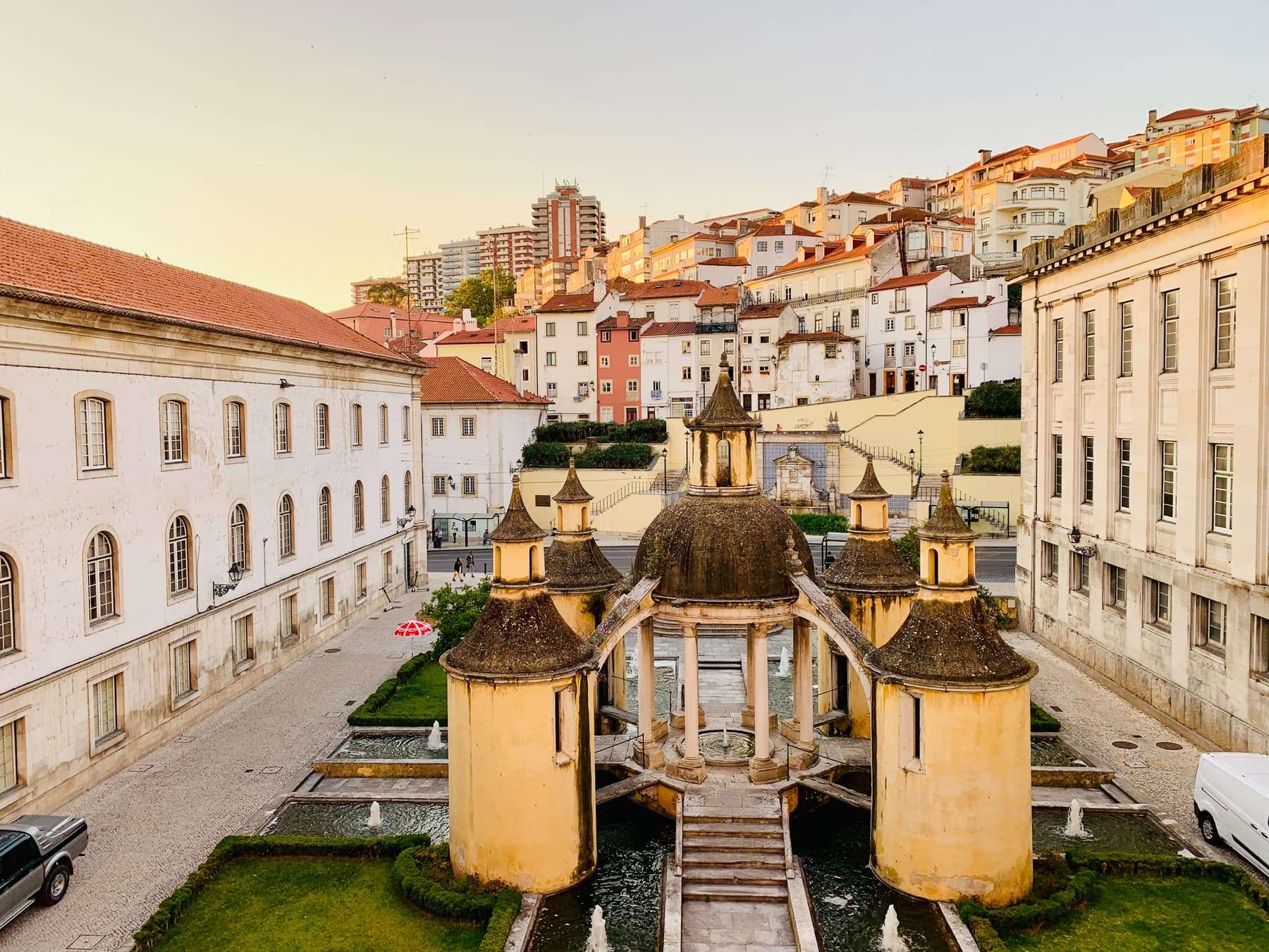 The hillside old town of Coimbra behind a domed garden fountain at golden hour