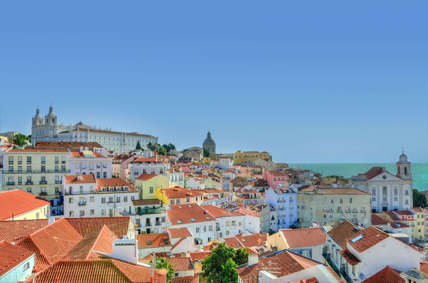 Terracotta rooftops of Lisbon's Alfama district with the Tagus estuary beyond