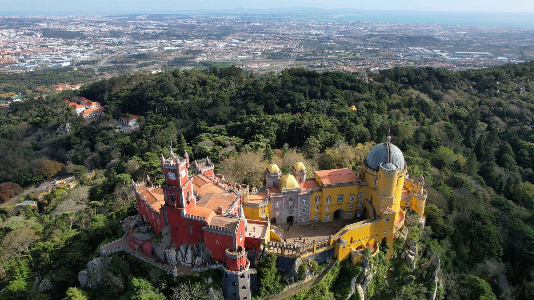Aerial view of the red and yellow Pena Palace on a wooded hilltop above Sintra