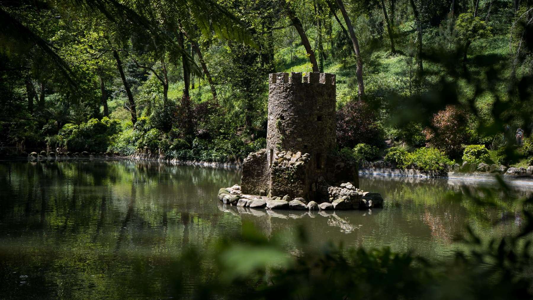 A small stone tower on a lake in the wooded Park of Pena, Sintra