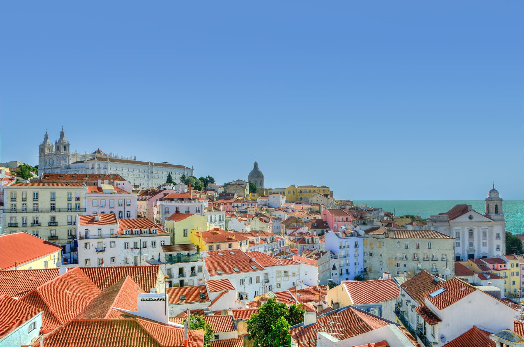 Terracotta rooftops of Lisbon's Alfama district with the Tagus estuary beyond