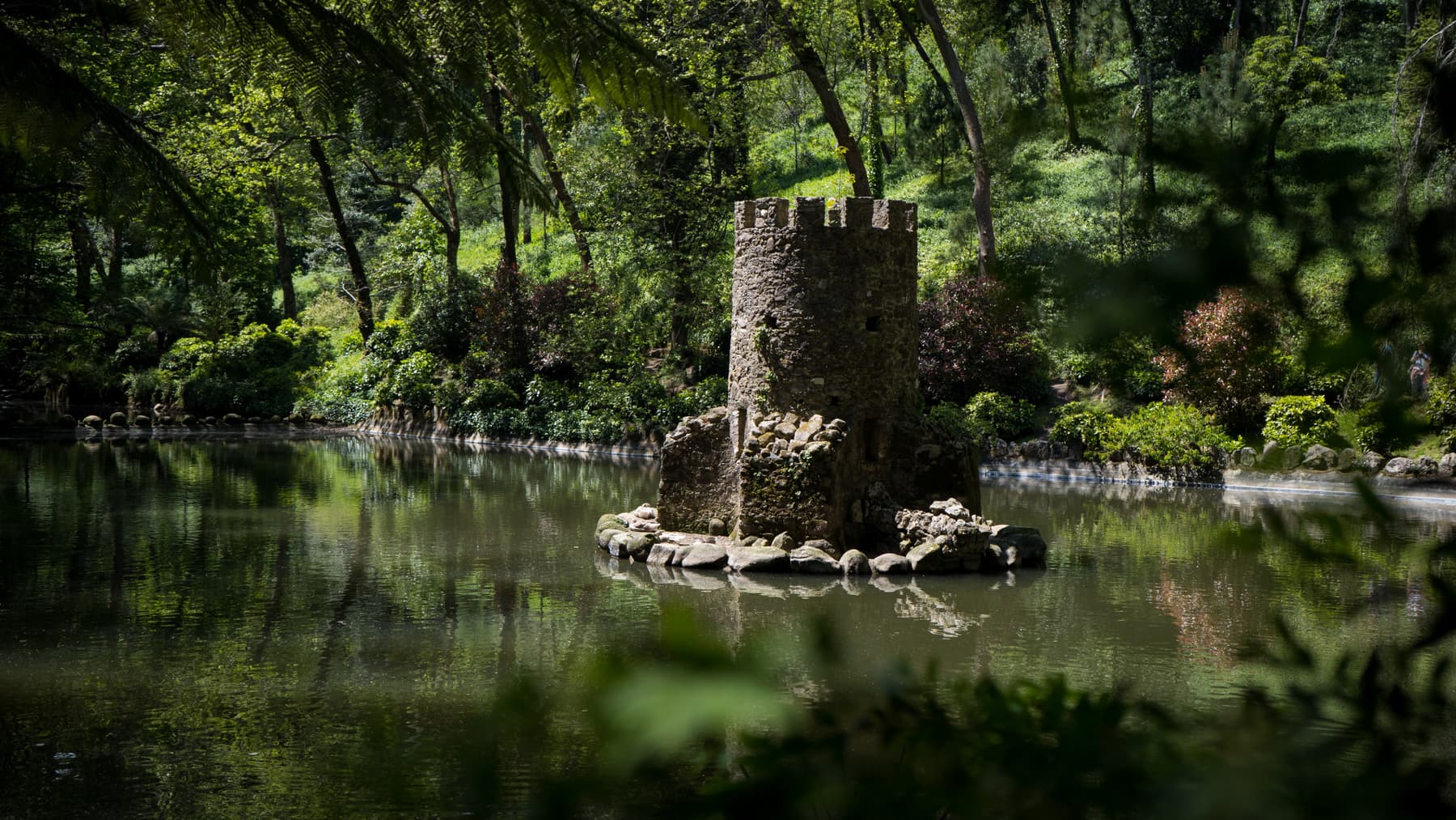 A small stone tower on a lake in the wooded Park of Pena, Sintra
